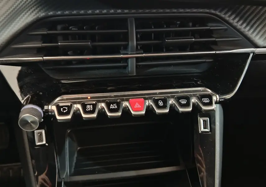 Vue rapprochée du tableau de bord noir de la Peugeot 208 blanche, avec boutons de commande et aérateurs visibles.