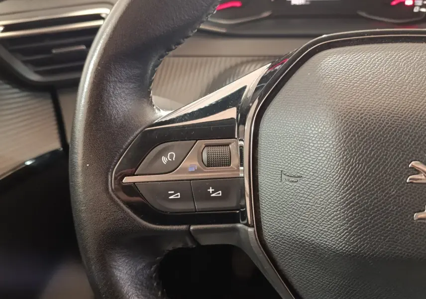 Gros plan sur le côté gauche du volant en cuir noir du Peugeot 208 blanc, avec commandes audio intégrées.