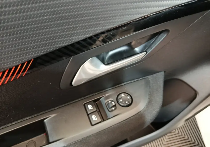 Gros plan sur la poignée intérieure et les commandes de vitres côté conducteur d'une Peugeot 208 blanche, finition Active Business.