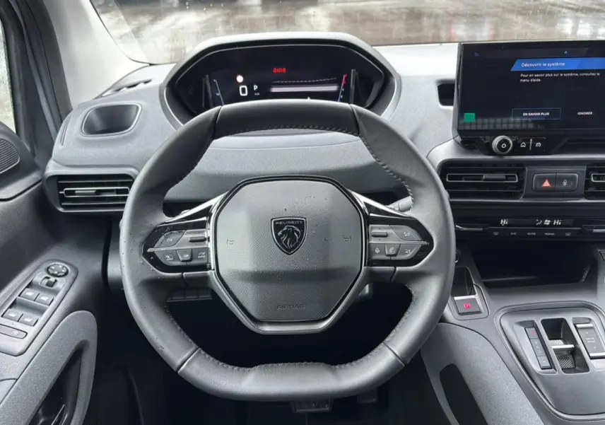 Vue intérieure centrée sur le volant cuir multifonctions du Peugeot Rifter 2025 avec tableau de bord digital et écran tactile.