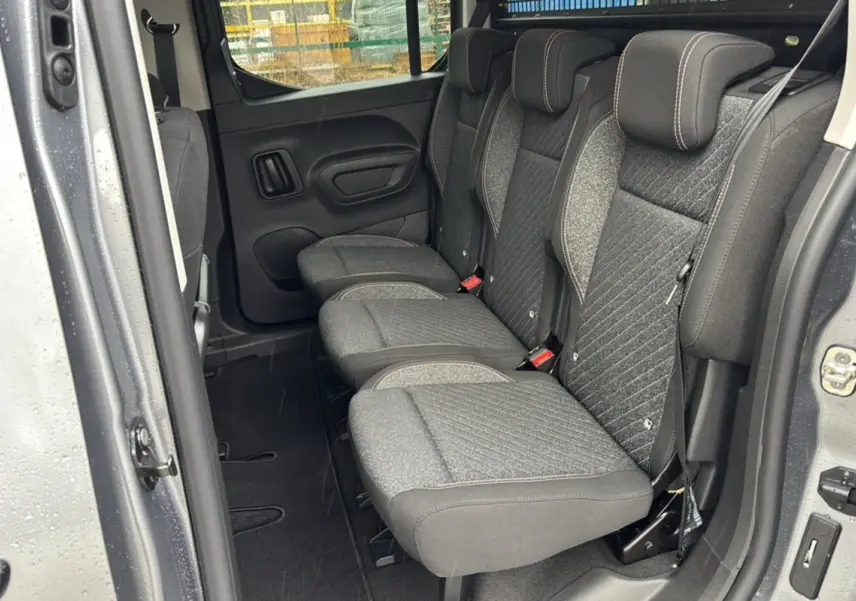 Vue latérale intérieure sur les sièges arrière tissu gris du Peugeot Rifter 2025 gris artense avec porte coulissante ouverte.