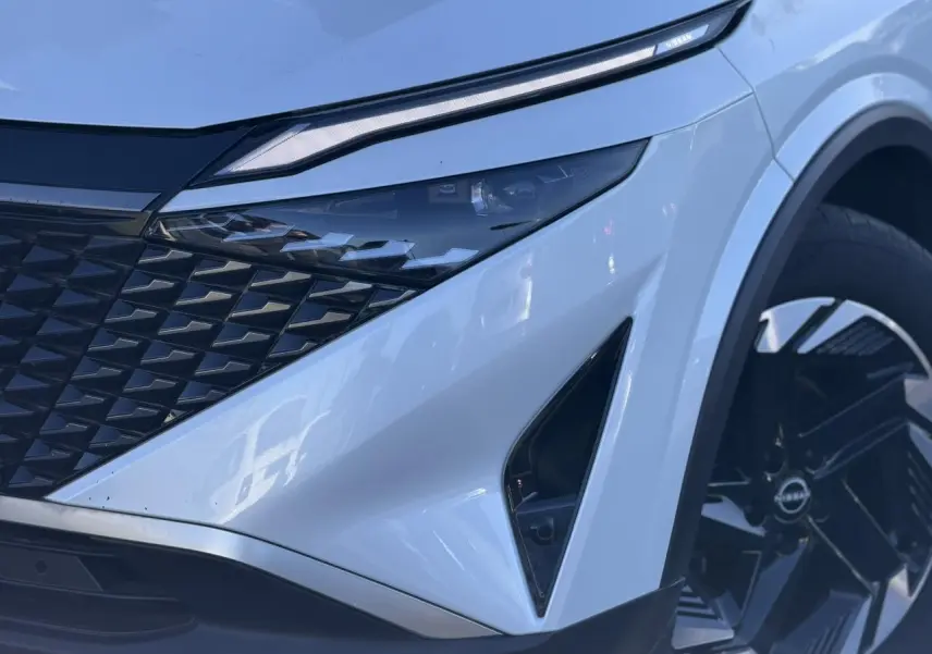 Gros plan sur l'avant droit du Nissan Qashqai blanc nacré, mettant en valeur le phare LED et la calandre noire.