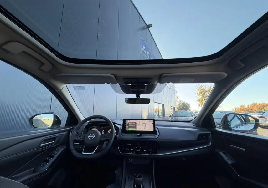 Vue intérieure avant du Nissan Qashqai 2025 avec toit panoramique en verre, tableau de bord numérique et écran tactile central.