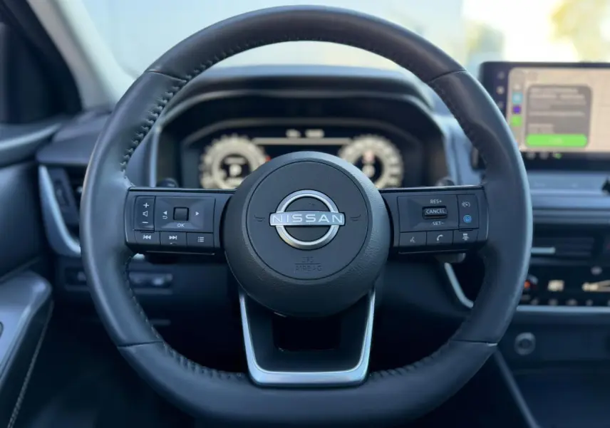 Vue frontale du volant cuir noir du Nissan Qashqai 2025 avec commandes intégrées et tableau de bord numérique flou.