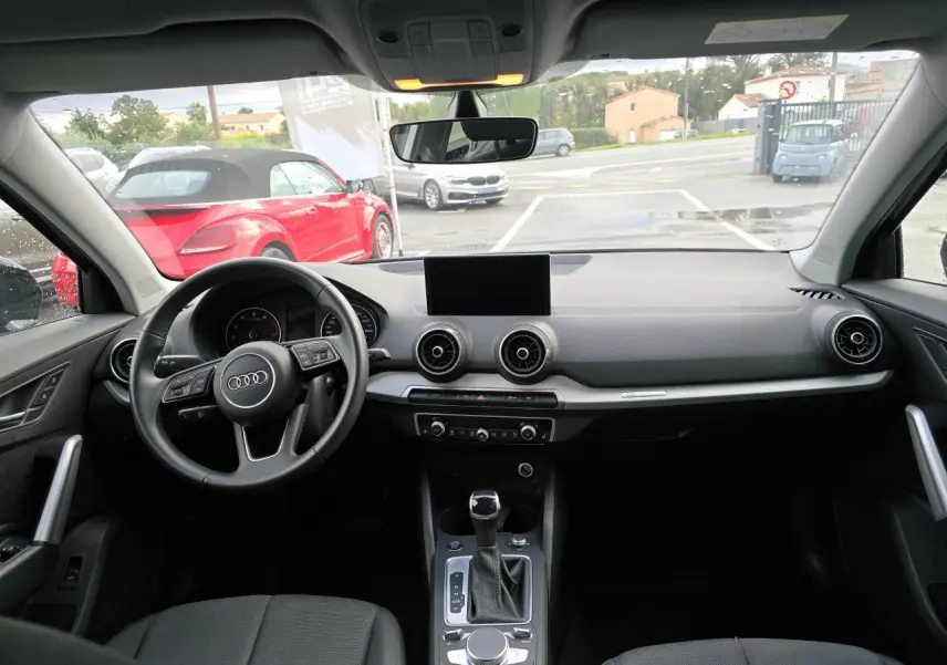 Vue intérieure avant de l'Audi Q2 2023 noir mythic, tableau de bord moderne avec écran central et volant multifonction cuir.