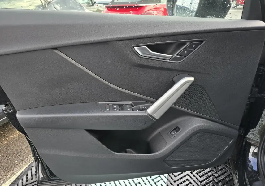Vue rapprochée de la porte avant gauche noire mythic de l'Audi Q2 35 TFSI avec commandes de vitres et poignée argentée.