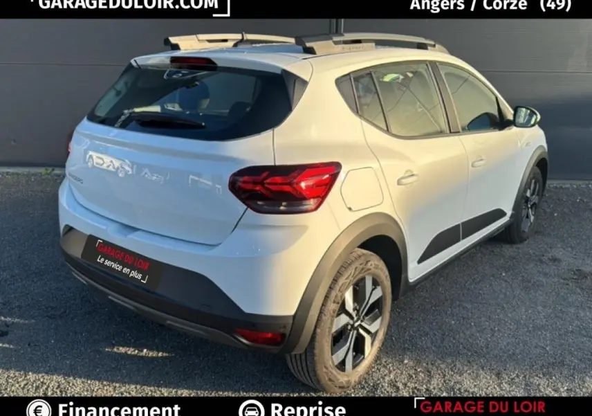 Vue 3/4 arrière droite d'une Dacia Sandero Expression blanche 2025 avec jantes noires et protections latérales noires.