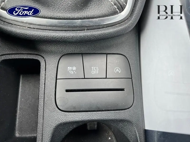 Gros plan sur les commandes centrales noires du Ford Fiesta blanc Glacier, avec bouton TCS OFF et fonction arrêt auto moteur.