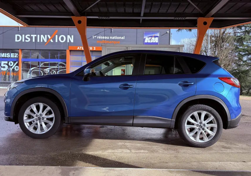 Vue latérale droite d'un Mazda CX-5 bleu 2013, soulignant ses jantes alliage et ses protections noires sur les bas de caisse.