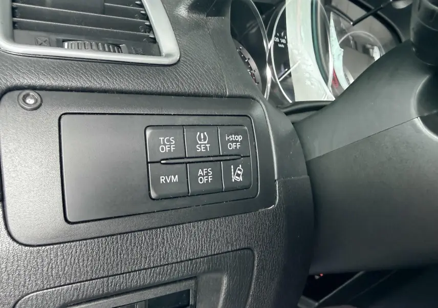 Gros plan sur les boutons de contrôle du tableau de bord côté gauche du Mazda CX-5 bleu, avec compteurs partiellement visibles.