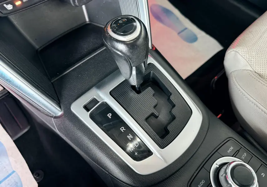 Gros plan sur le levier de vitesses automatique noir et argenté du Mazda CX-5 bleu, avec console centrale et siège clair partiel visible.