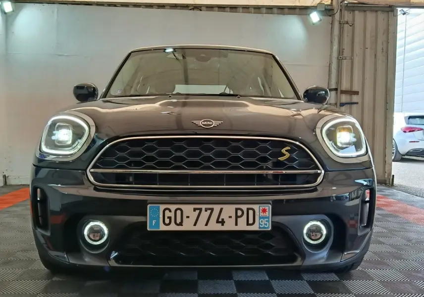 Vue frontale d'un MINI Countryman Cooper SE noir avec phares LED allumés et calandre hexagonale distinctive.