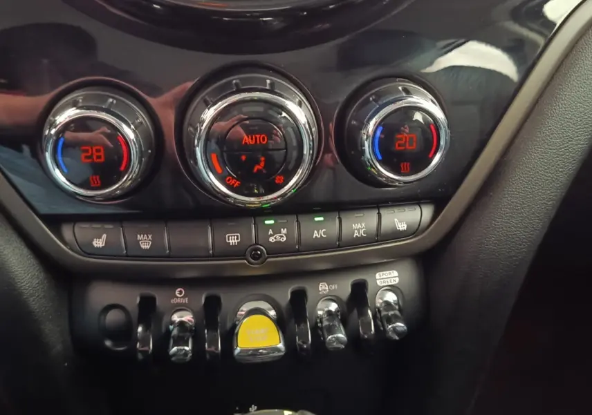 Gros plan sur la console centrale du MINI Countryman noir, montrant les commandes de climatisation et le bouton start/stop jaune.