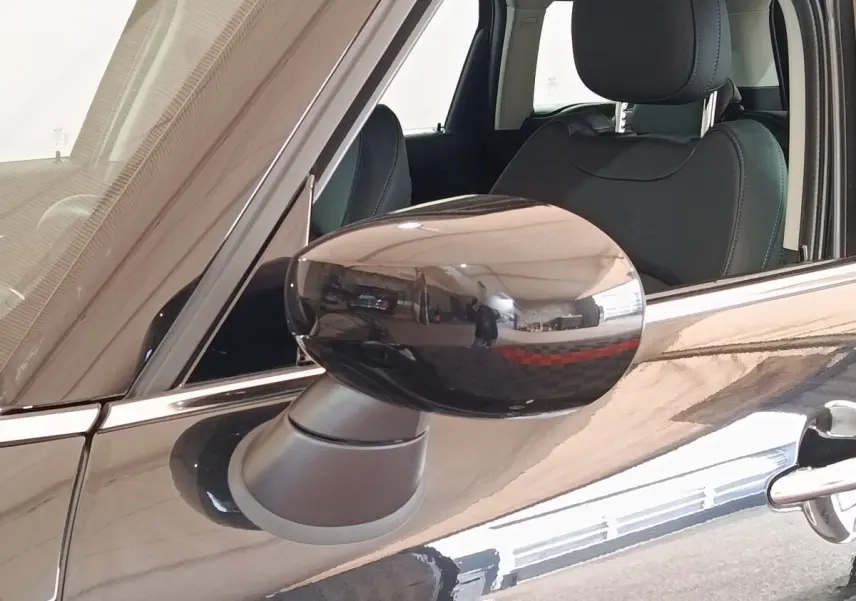 Gros plan sur le rétroviseur côté gauche noir brillant du MINI Countryman Cooper SE 2023 avec intérieur en cuir noir visible.
