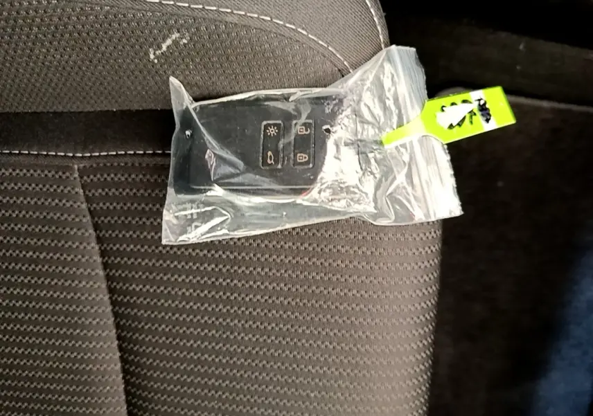 Télécommande Renault Megane Business E-Tech hybride blanche dans un sachet plastique posée sur un siège tissu gris foncé.