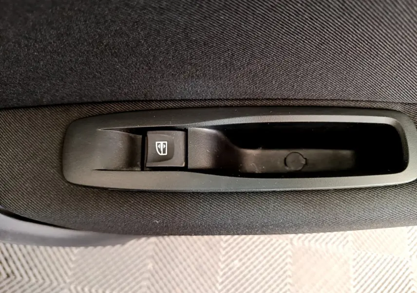 Gros plan sur le bouton de commande de la vitre électrique arrière dans la porte intérieure noire d’une Renault Megane blanche.