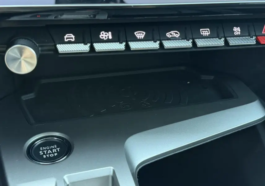 Détail intérieur du Peugeot 308 Hybrid 2025 montrant la zone de charge sans fil et le bouton start/stop, finition noire.