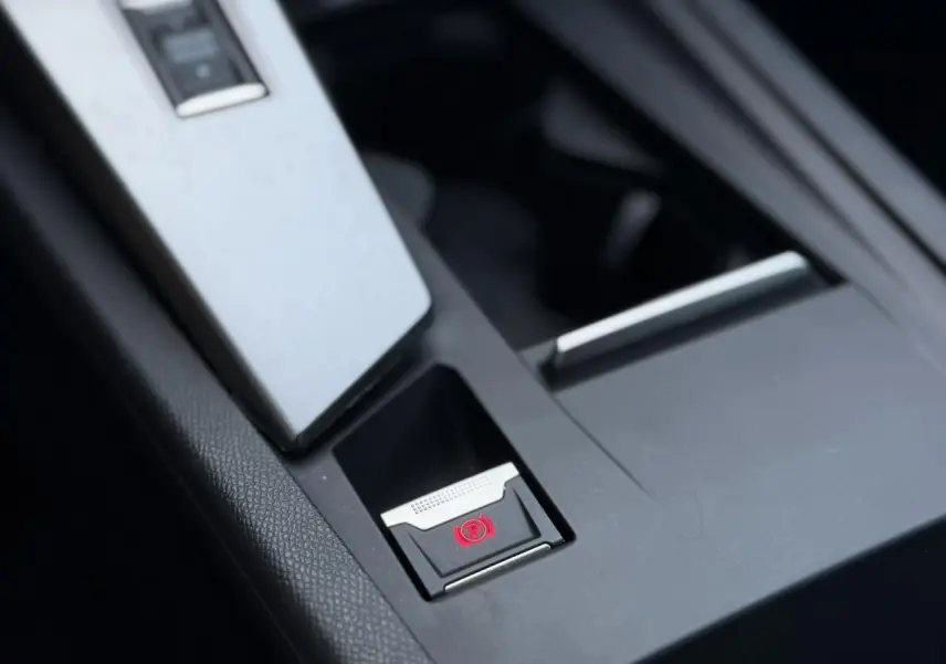 Gros plan sur la console centrale noire de la Peugeot 308 Hybrid avec bouton de frein de parking électronique éclairé en rouge.