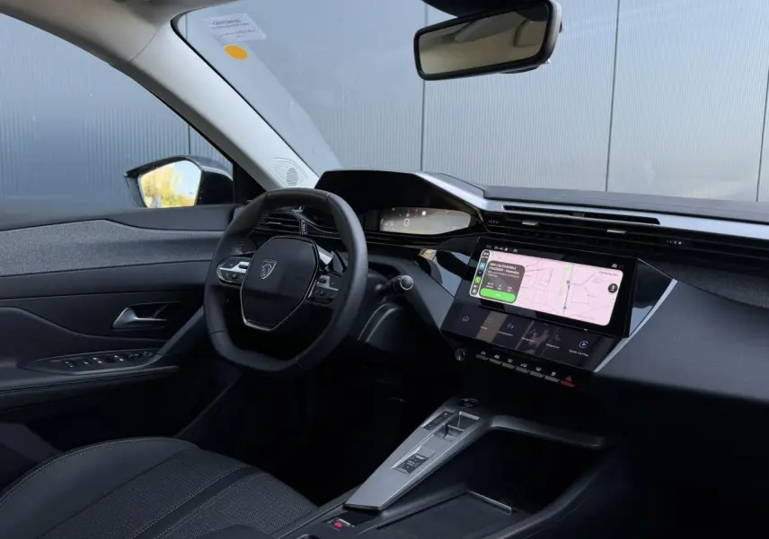 Vue intérieure côté conducteur de la Peugeot 308 Hybrid noire, avec tableau de bord numérique et écran tactile central affichant la navigation.