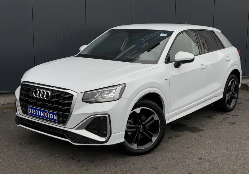 Audi Q2 30 TFSI S-Line blanc Glacier en 3/4 avant, avec jantes noires à 5 branches doubles et calandre noire.