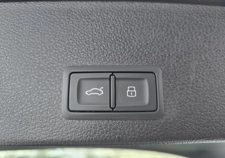 Boutons d'ouverture du coffre et de verrouillage intégrés dans le revêtement intérieur noir du hayon d'un Audi Q2 noir Mythic 2023.