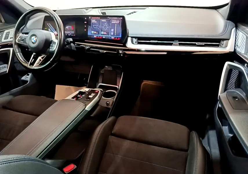 Intérieur avant BMW X1 xDrive23i M Sport 2023, vue du tableau de bord et volant cuir, écran tactile large et console centrale noire.