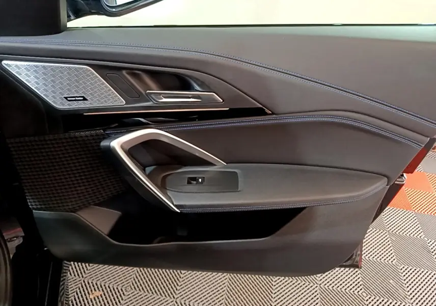 Détail de la porte côté gauche noire du BMW X1 2023 avec surpiqûres bleues et haut-parleur Harman Kardon intégré.