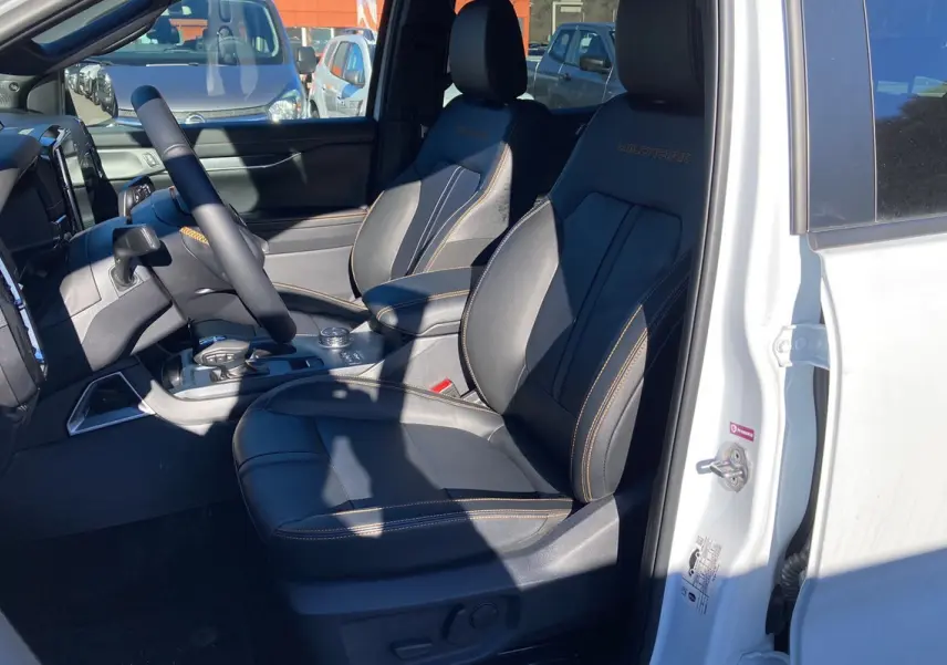 Vue intérieure côté conducteur du Ford Ranger blanc glacier 2025, sièges cuir noirs avec surpiqûres orange Wildtrak.