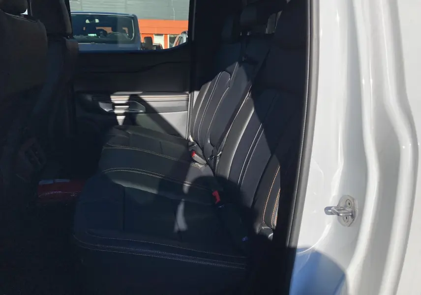 Vue intérieure côté droit sur la banquette arrière en cuir noir avec surpiqûres orange du Ford Ranger blanc glacier.