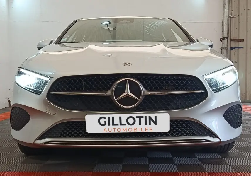 Vue frontale d'une Mercedes Classe A 250 e Business Line gris clair avec phares LED allumés et calandre noire ajourée.