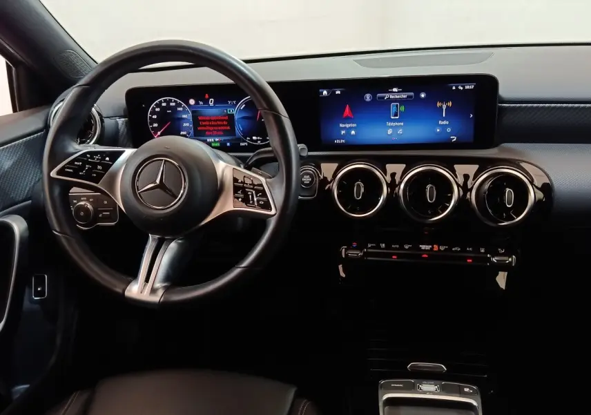 Vue intérieure centrée sur le volant cuir et alu, tableau de bord numérique et écran tactile de la Mercedes Classe A 250 e gris clair.