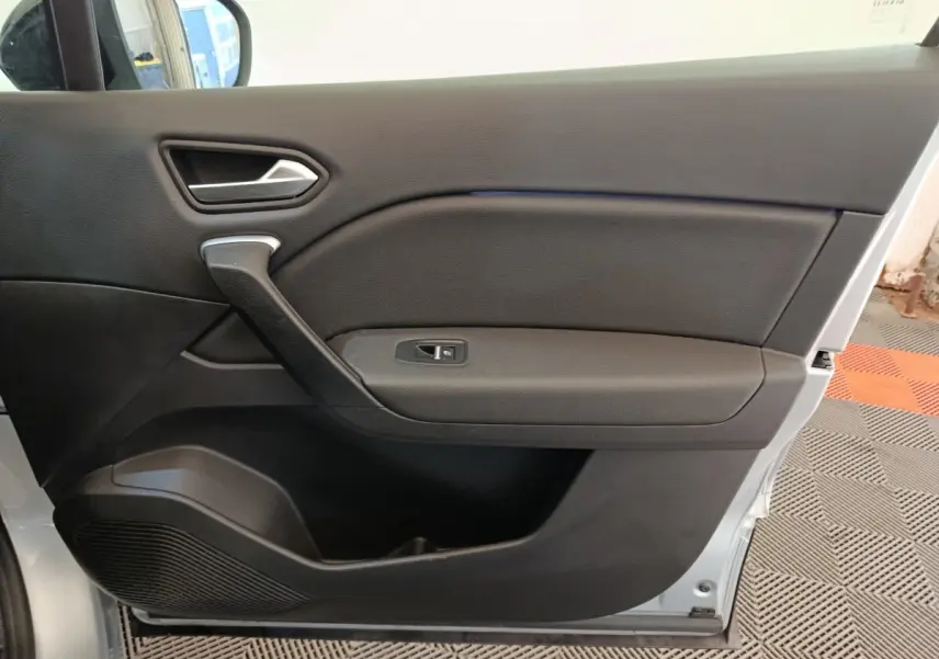 Vue intérieure de la porte avant gauche du Renault Captur gris clair, avec poignée et commande de vitre électrique.