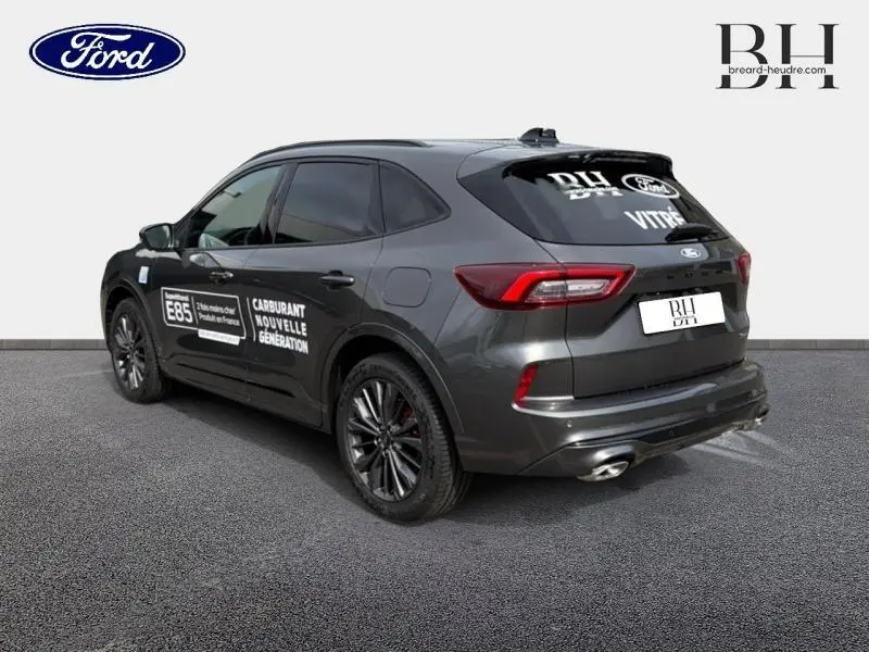 Vue 3/4 arrière droite du Ford Kuga gris Magnetic avec marquages publicitaires sur la porte et jantes noires.