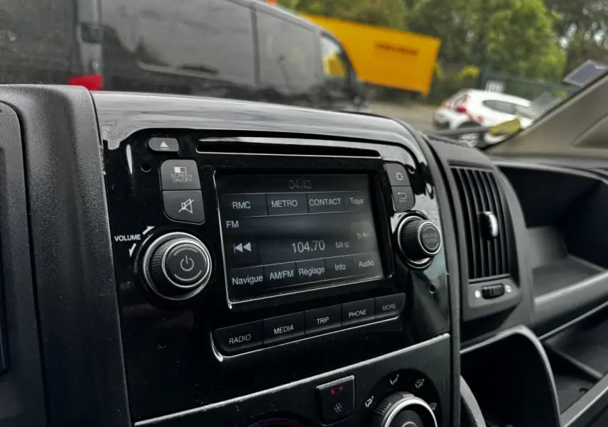 Gros plan sur la console centrale noire du Citroën Jumper blanc, affichant l’écran tactile radio FM à 104,7 MHz.