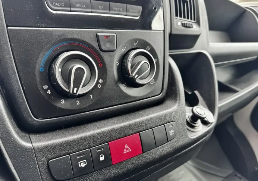 Gros plan sur les commandes de climatisation et les boutons de sécurité du tableau de bord noir du Citroën Jumper blanc.