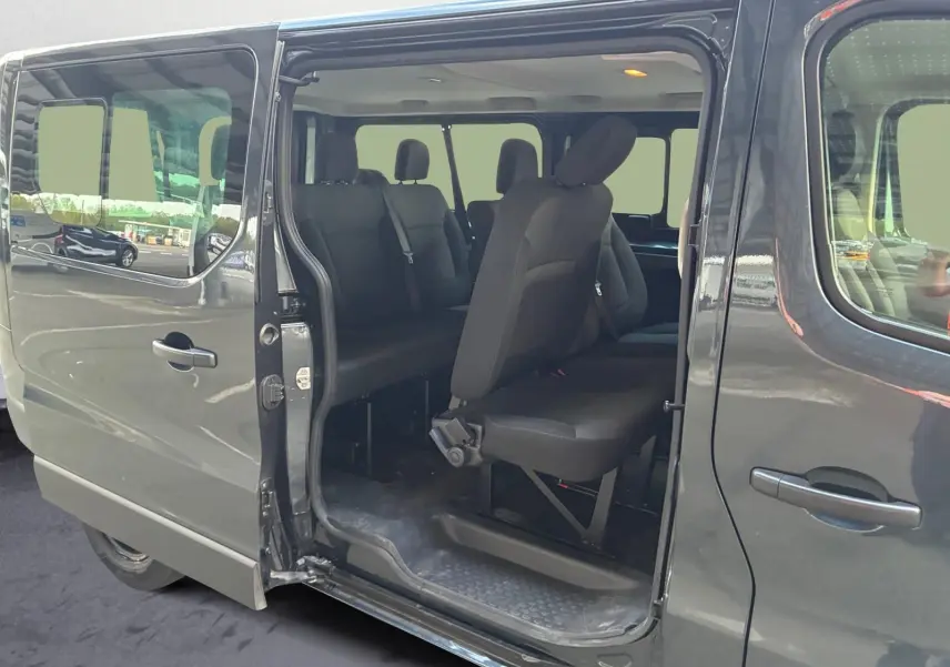 Vue latérale gauche du Renault Trafic Combi gris foncé avec porte coulissante ouverte révélant les sièges passagers noirs.