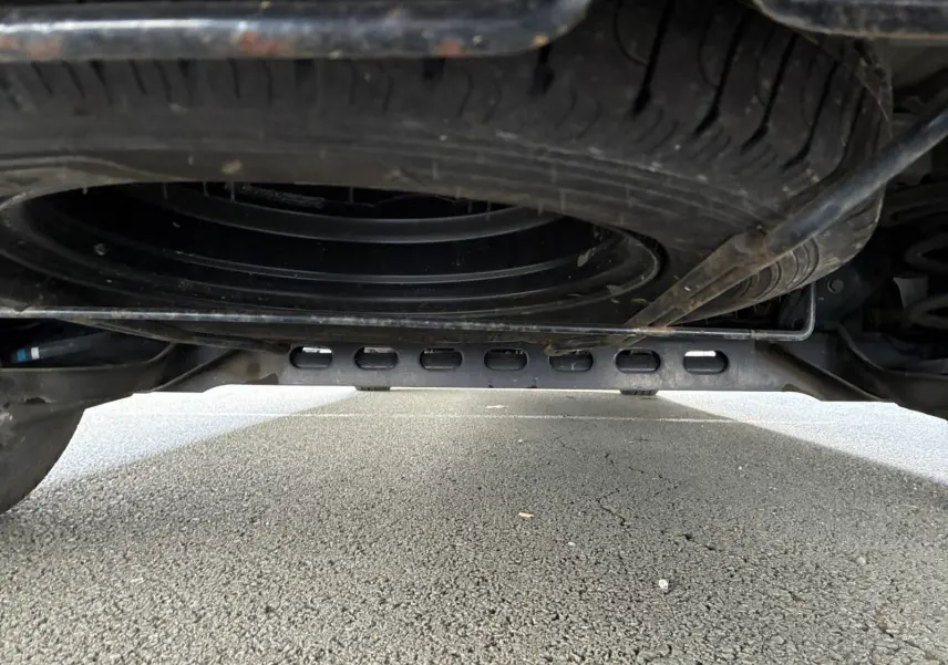 Vue en contre-plongée sous un Renault Trafic Combi gris foncé, montrant la roue de secours et le châssis métallique.