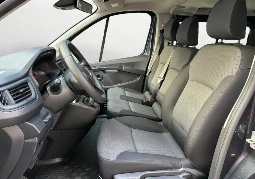 Vue intérieure côté conducteur du Renault Trafic Combi 2023, sièges tissu gris et tableau de bord noir.