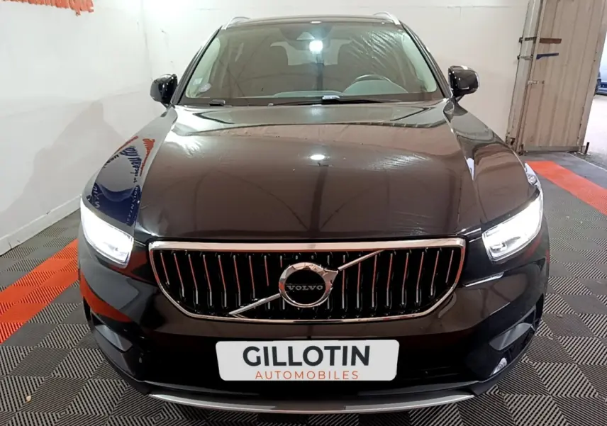 Vue frontale d'un Volvo XC40 noir avec calandre verticale chromée et phares LED allumés en intérieur showroom.