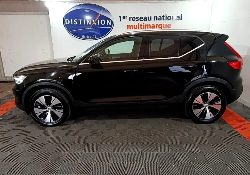 Profil côté gauche d'un Volvo XC40 noir hybride rechargeable, avec jantes modernes et lignes épurées en intérieur showroom.