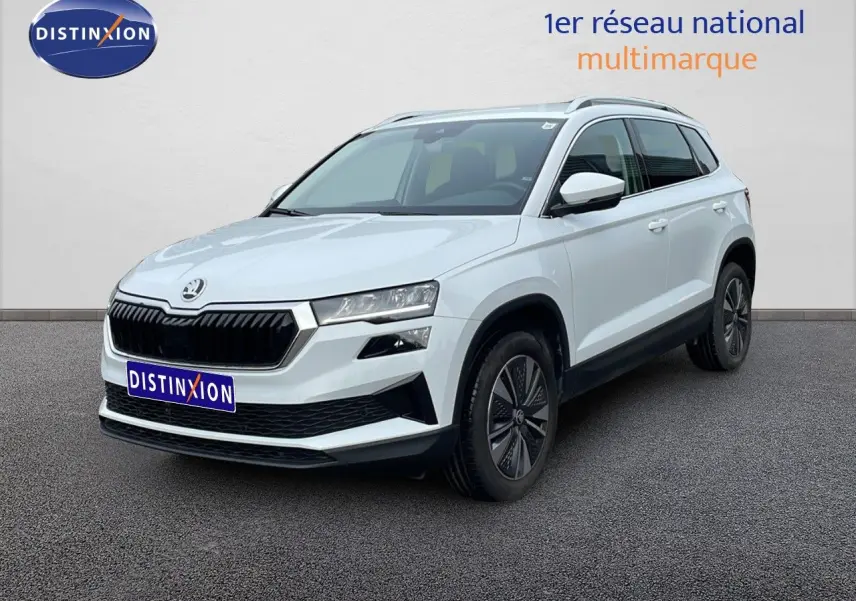 Vue 3/4 avant d’un Skoda Karoq blanc glacier avec calandre noire et jantes bi-ton, sur fond neutre extérieur.