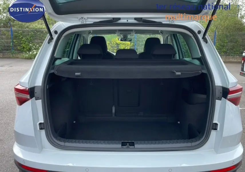 Vue arrière ouverte du coffre d’un Skoda Karoq blanc glacier 2025, montrant l’espace de chargement vide et la plage arrière noire.