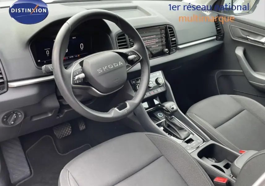 Vue intérieure côté conducteur du Skoda Karoq blanc glacier 2025, avec tableau de bord numérique et volant multifonction cuir.