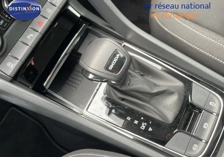 Gros plan sur le levier de vitesse automatique SKODA dans l’habitacle du KAROQ, avec sellerie tissu gris et coutures blanches.