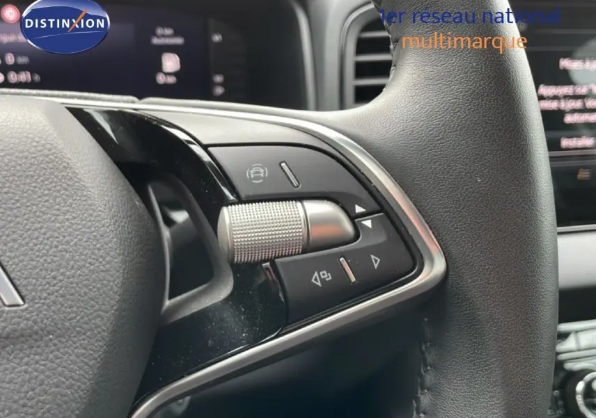 Gros plan sur les commandes au volant cuir noir du Skoda Karoq blanc glacier, avec tableau de bord numérique en arrière-plan.