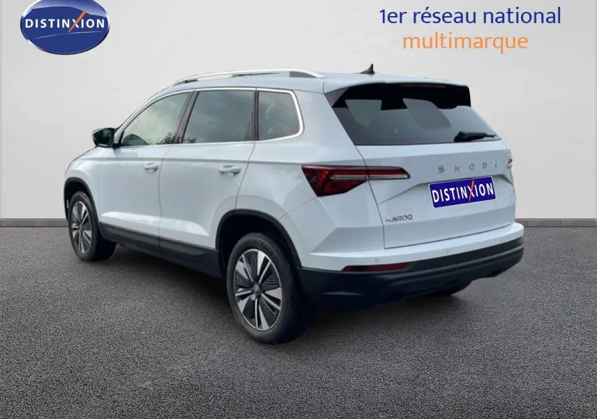 Vue 3/4 arrière droite d'un Skoda Karoq blanc glacier avec jantes bi-ton et vitres teintées.