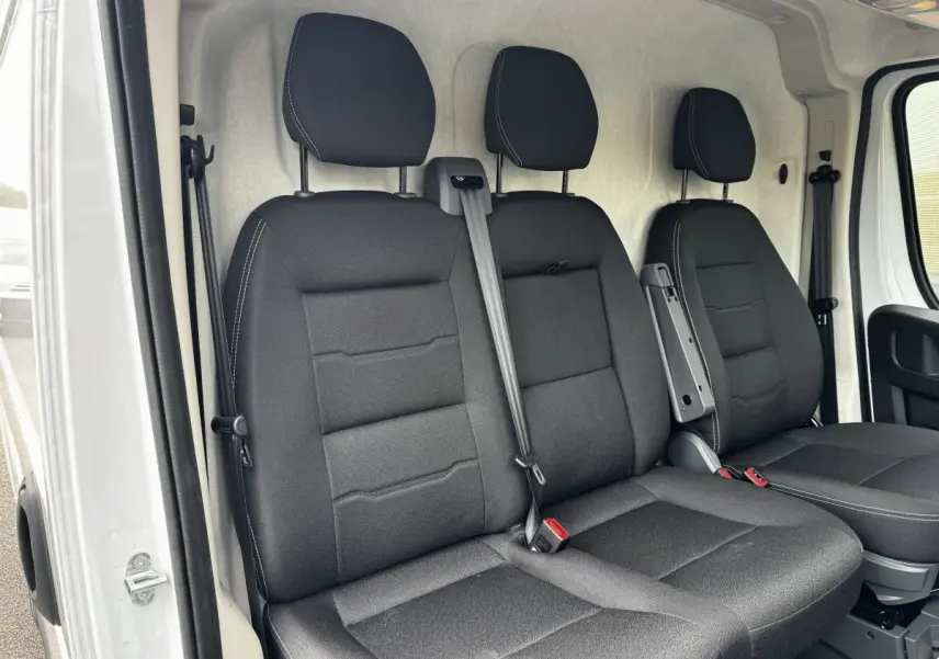 Vue intérieure côté conducteur du Peugeot Boxer Fourgon blanc 2026, montrant les sièges avant noirs avec accoudoir central.