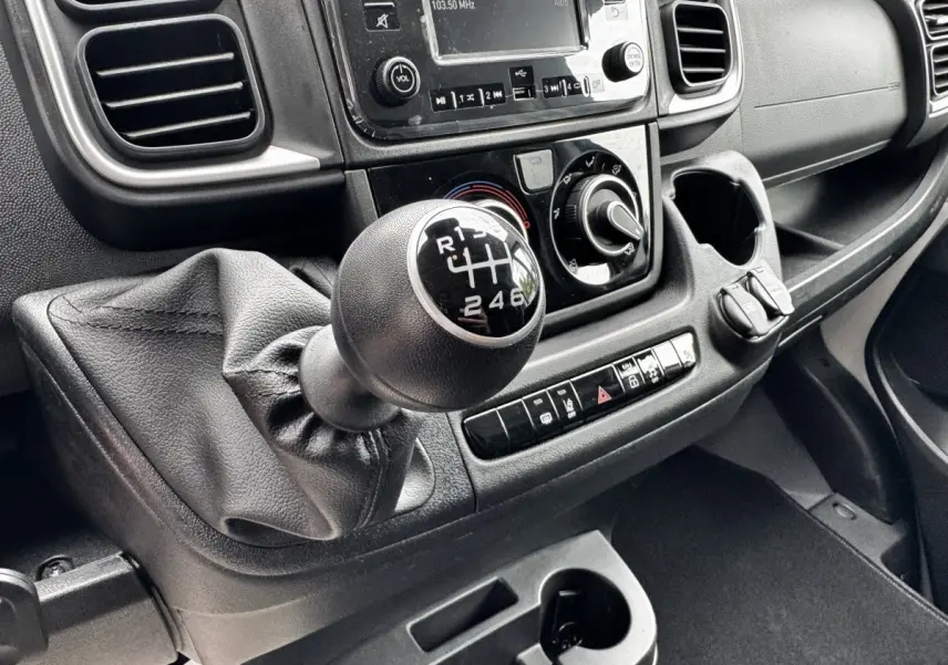 Gros plan sur le levier de vitesses manuel noir du tableau de bord du Peugeot Boxer Fourgon blanc, avec commandes et écran tactile.