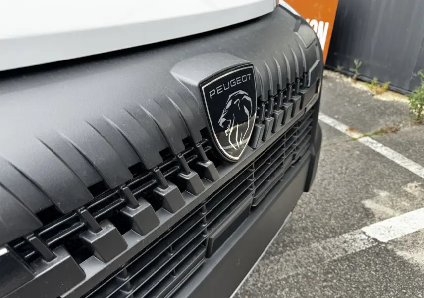 Gros plan sur la calandre noire et le logo Peugeot du Peugeot Boxer Fourgon blanc, vue avant rapprochée.