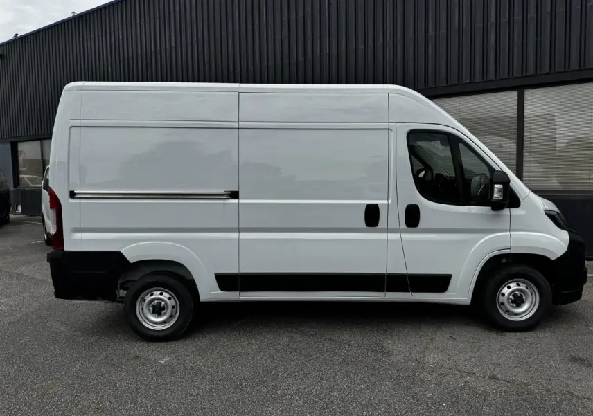 Vue de profil côté gauche d’un Peugeot Boxer Fourgon blanc avec porte coulissante et protections noires sur un parking.